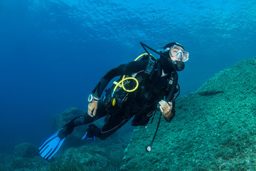 woman scuba diving over rocks in the Mediterranean Sea