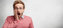 Horizontal Shot Of Amazed Stupefied Bearded Male Wonk Wears Spectacles, Looks With Shocking Expression, Keeps Mouth Widely Opened, Being Frightened See Car Accident On Street, Isolated On White Wall