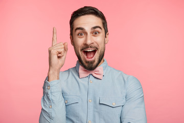 Studio shot of intelligent bearded man raises fore finger as recieves good idea or glad find out about successfully passed exam. Excited cheerful man remembers something pleasant, isolated on pink