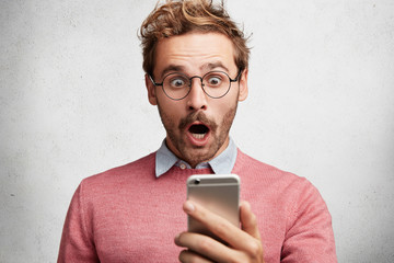 Wall Mural - Shocked bearded male model surprised to recieve text message about his bills, realize that he is complete bankrupt, has no money to pay debts. Stunned man reads unexpected news online on mobile phone