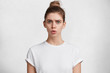 © WHstudio Leushin N - Horizontal shot of shocked puzzled discontent beautiful young female has dark hair tied in knot, wears casual white t shirt, scared of hearing awful news, models against white studio background.