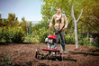 Happy man Farmer plows the land with a cultivator, preparing it for planting vegetables, on a sunny day garden