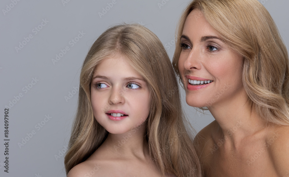 Joyful attractive mother and her adorable little daughter are standing together with naked