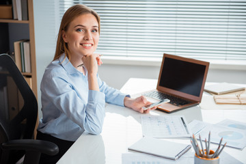 Poster - Portrait of cheerful businesswoman typing in mobile smartphone while locating at table in office. Occupation concept