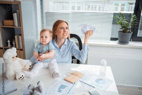 Fotografia, Obraz Portrait of angry businesswoman crumpling paper while holding serene kid in hand