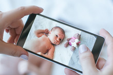 Mother Takes A Photo Of Her Newborn Baby On A Smartphone. Family Memories.
