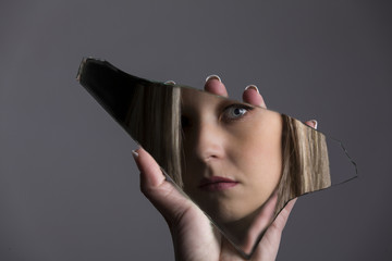 Woman looking at her face in shard of broken mirror