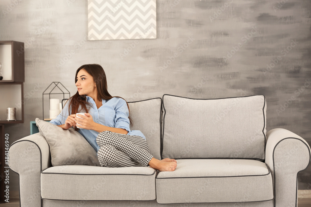 Young woman with cup of tea on sofa at home