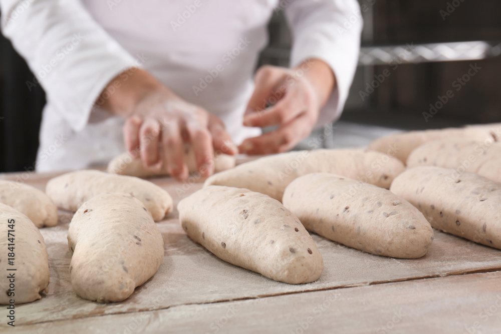 Raw loaves of bread on table and man in bakery