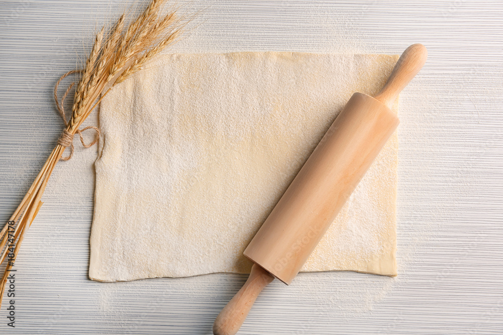 Raw puff dough, rolling pin and wheat spikes on table