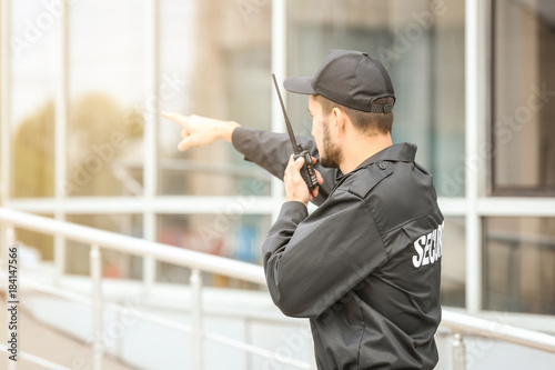 Male security guard using portable radio transmitter near building outdoors Poster Mural XXL