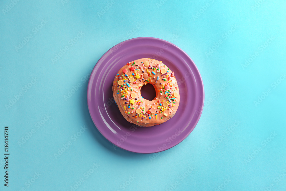 Plate with tasty donut on color background