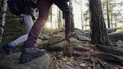 stylish travelers climbing rocks in forest