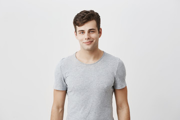 Wall Mural - Stylish caucasian man with appealing blue eyes smiling into camera having pleased expression, glad to meet his girlfriend. Hipster in gray t-shirt grinning having cheerful look. Positive emotions