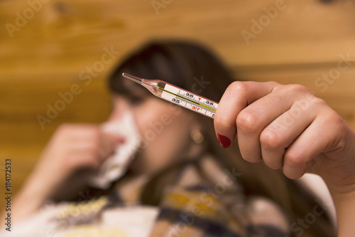 Fotografia Sick woman in her bed looking at a clinical thermometer