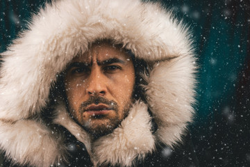close up portrait of a white man dressed with an eskimo jacket in the snow looking at the camera