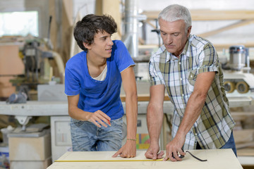 senior and junior carpenters measuring wood