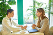 © Seventyfour - Side view portrait of two modern young women discussing work sitting at table in cafe during business meeting or job interview