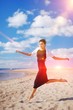 © raisondtre - Magnificent portrait of young slim woman in a black dress, a figure-hugging, running barefoot on the sand, arms outstretched, on a background of blue sky and floating on it white clouds.