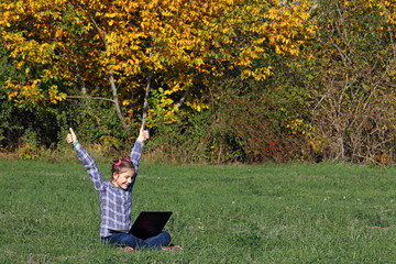 Wall Mural - happy little girl with thumbs up and a laptop in the park