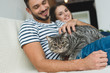© LIGHTFIELD STUDIOS - happy young couple with adorable tabby cat sitting on couch