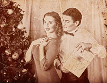Christmas Nostalgy Couple On Party Near Xmas Tree Take Gift Box. Happy Family On Holiday. Vintage Sepia Old Retro Photo 1910-1940.