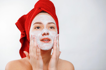 Wall Mural - happy beautiful girl with a red towel on her head applies a scrub on the face of a large portrait on a white background