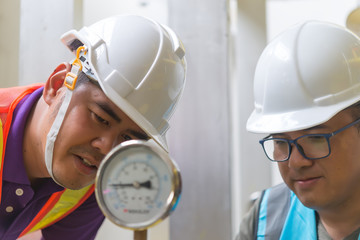 Two Asian engineer working in the boiler room,maintenance checking technical data of heating system equipment,Thailand people,Discuss the issue about the pipe pressure.