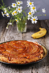 Wall Mural - Traditional homemade banana caramel pie on vintage wooden table decorated a bouquet of chamomiles.  Upside down banana cake. Selective focus 