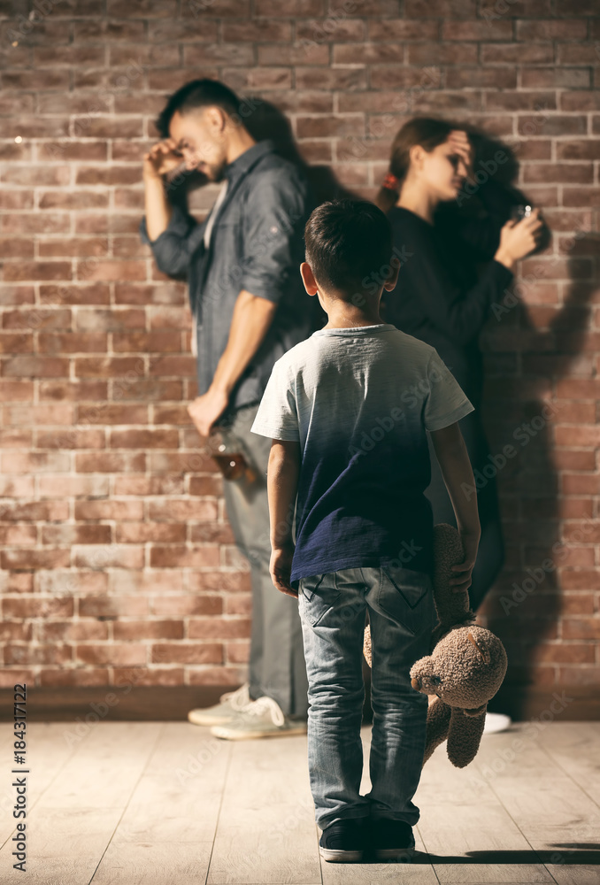 Little boy holding teddy bear while his parents having quarrel on background