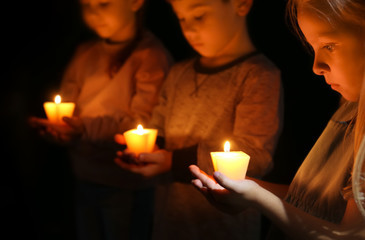 Little children holding burning candles in darkness