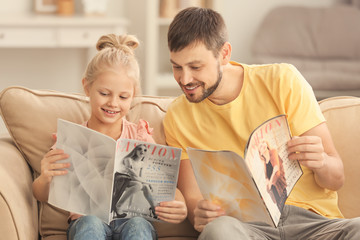 Wall Mural - Cute little girl and her father reading magazines at home