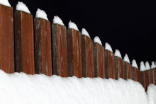 Part Of The Wooden Fence Of The Backyard Is Covered With Snow At Night.