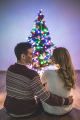 The happy couple sit on the floor near the christmas tree