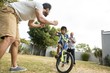 © wavebreak3 - Father and grandfather cheering for boy cycling in yard