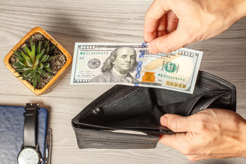 Man's hands holding empty black leather wallet and 100 dollar bill