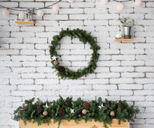 Closeup View Of Round Elegant Christmas Wreath Hanging On White Brick Wall. Wreath Decorated With Ratten Balls, Dried Flowers Of Lotus And Wooden Star. Beautiful Long Garland On Top Of Fireplace.