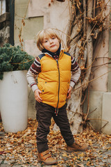 Wall Mural - Outdoor portrait of a cute little boy of 4-5 years old, wearing warm yellow vest