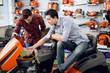 © VadimGuzhva - A consultant in a garden tools store shows a customer a lawn mower.