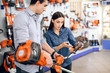 © VadimGuzhva - The seller in the store shows the customers a grasscutter.
