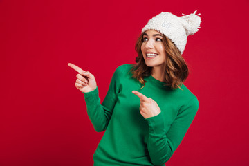 Wall Mural - Smiling brunette woman in sweater and funny hat pointing away