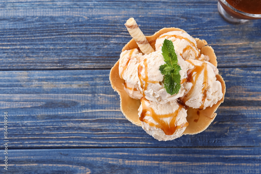 Delicious ice cream with caramel topping in waffle bowl on table