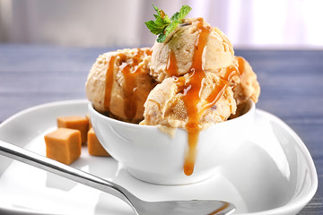 Wall Mural - Bowl of delicious ice cream with caramel topping on plate, closeup