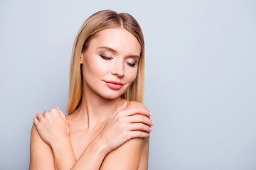 Close up portrait of gorgeous delightful charming young pretty happy woman with perfect bode, skin and hair, she is touching her shoulders after aroma therapy. She is isolated on grey background