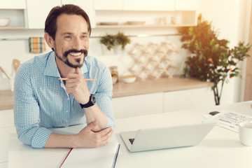 Wall Mural - Positive emotions. Cheerful happy nice man leaning on the table and smiling while being in a great mood