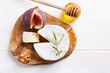 Cheese plate with brie, figs, honey and nuts on white table.