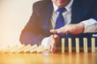 © EKKAPON - Businesswoman Hand Stopping Dominoes From Falling On Office Desk. Risk Prevention Concept