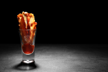 Wall Mural - Glass with cooked bacon rashers and sauce on table against black background