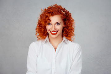 Happy and beautiful. Closeup head shot portrait, young business woman with curly hair in white shirt smiling isolated on gray grey wall background. Positive human emotion facial expression