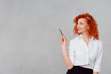 Happy business woman point pen at wall. Young lady smiling school teacher pointing at copy space or gray board with pencil.